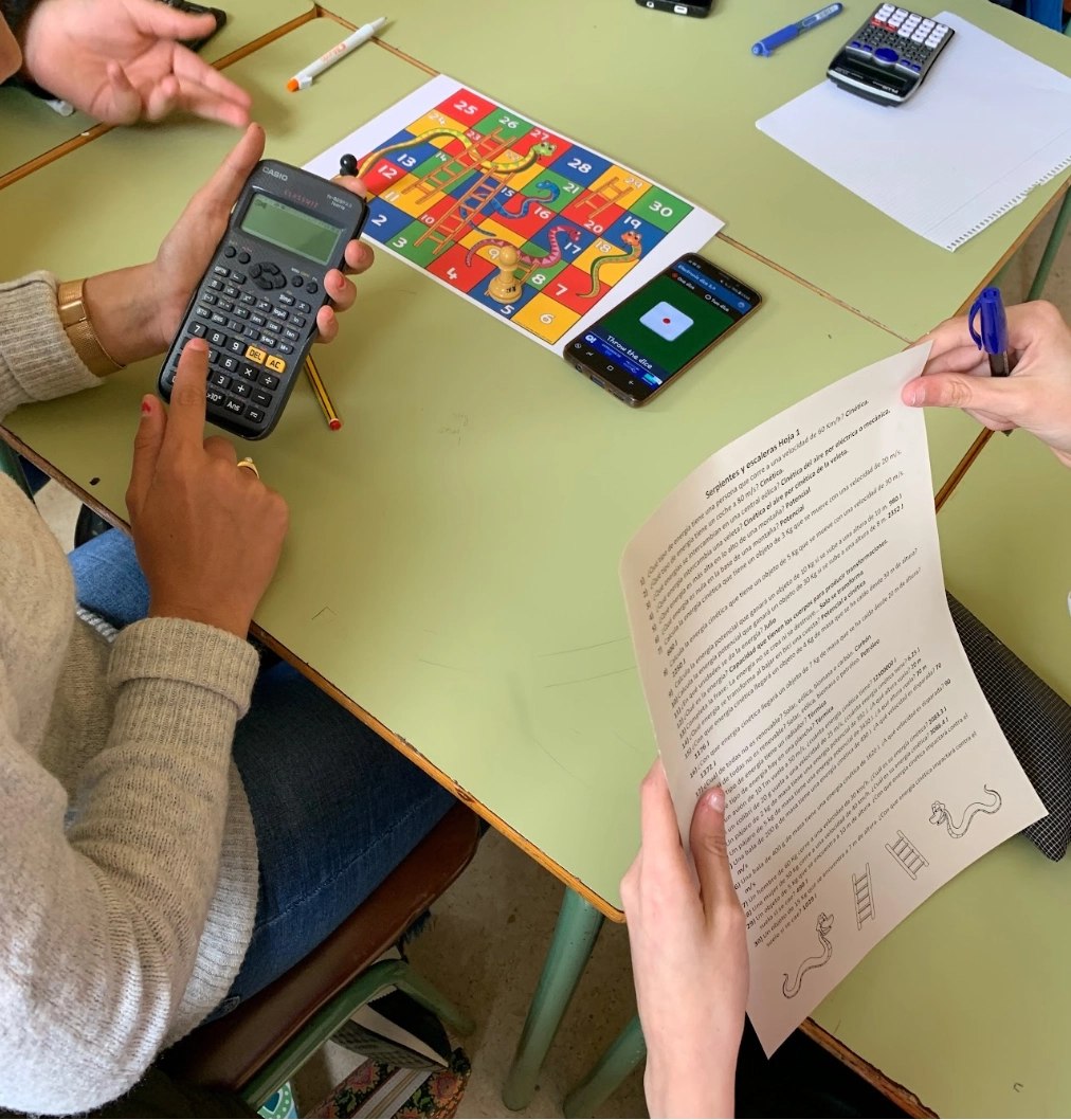 Alumnado jugando a serpientes y escaleras con el tablero, un dado virtual y la hoja de preguntas